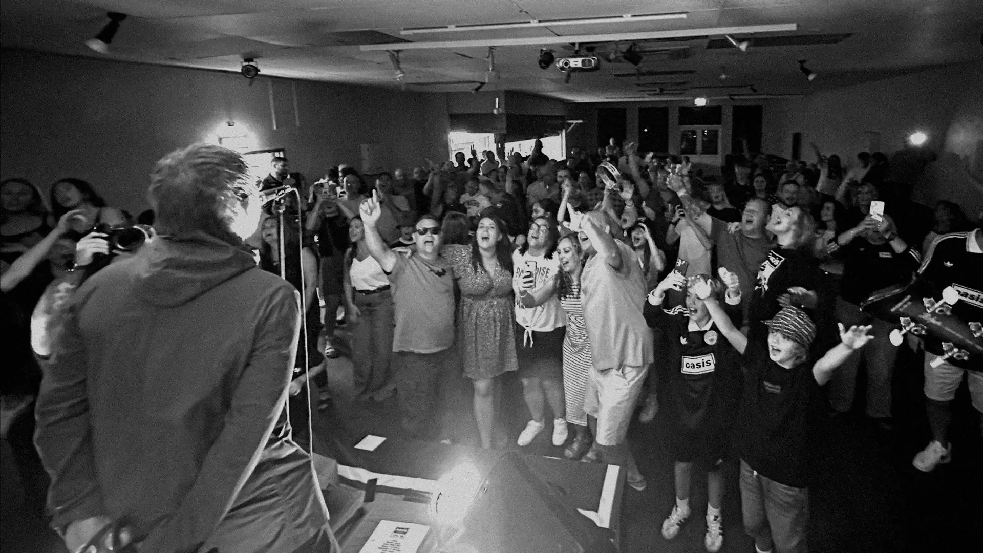 A packed crowd singing back to the Oasis Mornin' Glory frontman, seen from behind him on stage